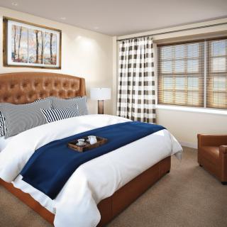 A cozy bedroom with a stylish bed, plaid curtains, and an armchair.