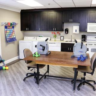 A multifunctional room featuring a kitchenette area with laundry facilities, therapy equipment, and a workspace.
