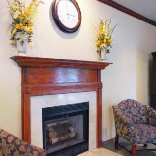 A cozy seating area featuring a wooden mantel adorned with floral arrangements and a clock above the fireplace.