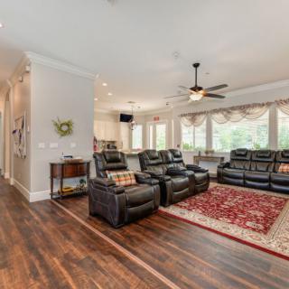 A spacious living room with recliner seating, a ceiling fan, and large windows offering plenty of natural light.