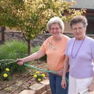 Two elderly women watering plants in a garden.
