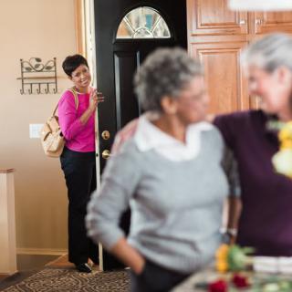 A woman enters a home where two other women are having a conversation.