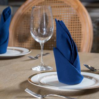 A sophisticated dining table setup with a blue napkin neatly folded on a plate alongside a wine glass.