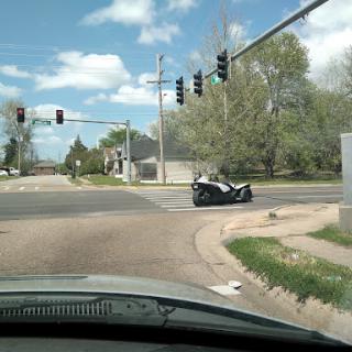 A motorcycle navigating an intersection with traffic lights on a cloudy day.