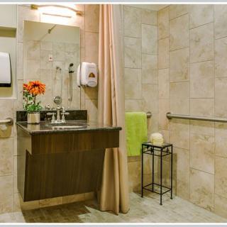 A modern bathroom with a sink, mirror, flower arrangement, and towel on a tiled wall.