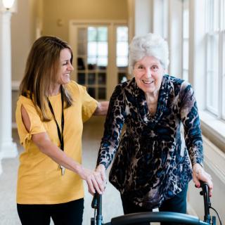 A caregiver assisting an elderly woman using a walker in a nursing home.