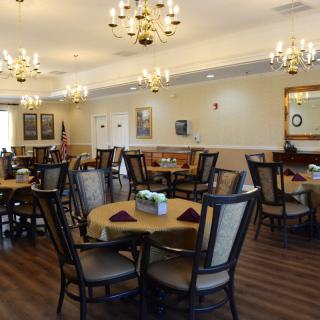 An elegant dining room with neatly arranged tables and chairs, illuminated by chandeliers.