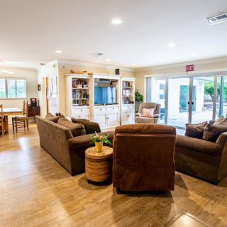 A cozy living room with comfortable sofas arranged around a center table, featuring a television and bookshelf in the background.