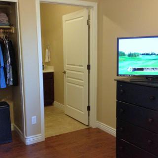 A bedroom with an open closet, a dresser topped with a television, and a view into an adjoining bathroom.