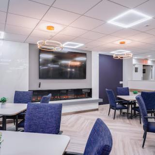 A modern conference room with blue chairs, tables, a large TV screen, and stylish lighting.