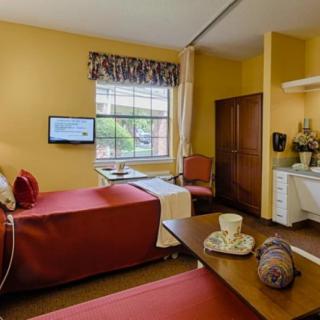 A cozy bedroom with twin beds, a TV mounted on the wall, and a small sitting area by the window.