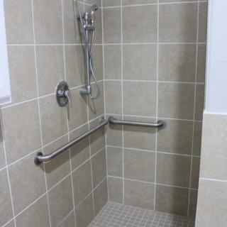 A tiled accessible shower with handrails and a showerhead.