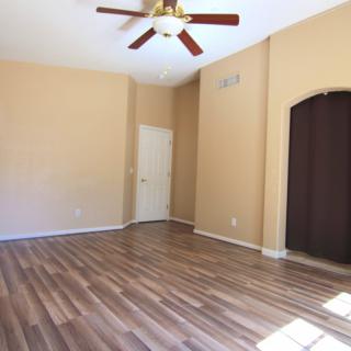 An empty room featuring a ceiling fan, hardwood floors, and beige walls.