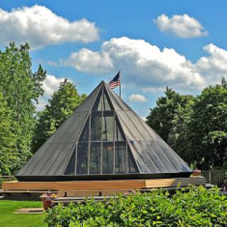 A modern glass pyramid structure set against a backdrop of lush greenery and a blue sky.