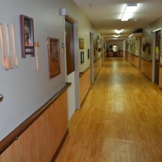 A well-lit hallway featuring wooden flooring, decorated walls, and several doors leading to individual rooms.