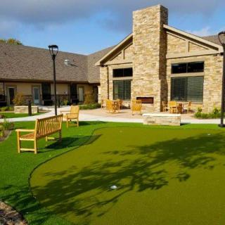 A modern stone building with a well-maintained backyard featuring benches and a green lawn.