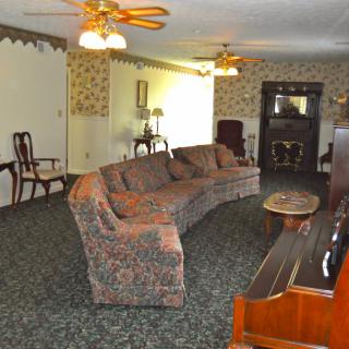 A vintage-style living room with patterned sofas, a piano, and a fireplace.