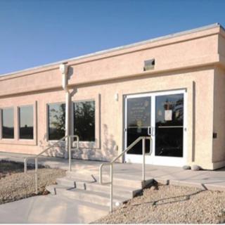 A small building with a glass door entrance, large windows, and a front staircase with handrails.
