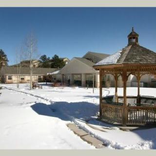 A snow-covered landscape featuring a wooden gazebo and buildings in the background.