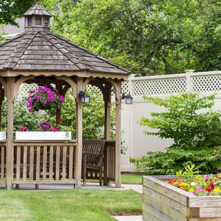 A picturesque garden with a wooden gazebo surrounded by vibrant flowers and greenery.