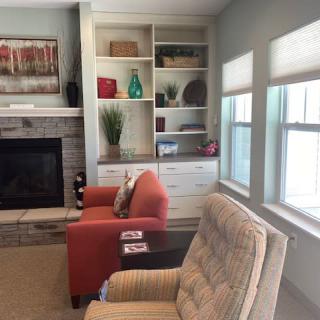 A cozy living room with armchairs, a fireplace, and decorative shelves by the window.