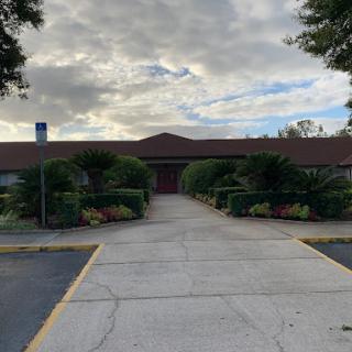 Entrance to a serene building surrounded by greenery under a cloudy sky.