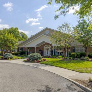 A charming single-story building surrounded by lush greenery and a well-maintained driveway under a clear blue sky.