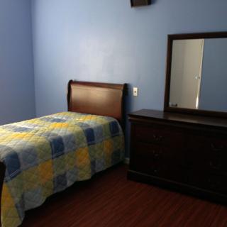 A minimalist bedroom with blue walls, featuring a single bed and wooden dresser with a mirror.