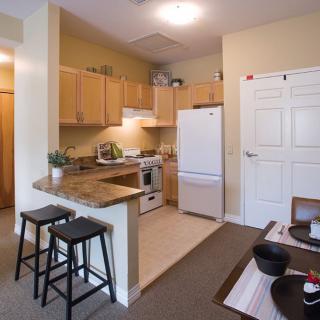A cozy apartment kitchen with wooden cabinets, a white refrigerator, and seating at the countertop.