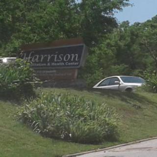 A view of the Harrison sign with a car parked nearby amidst greenery.