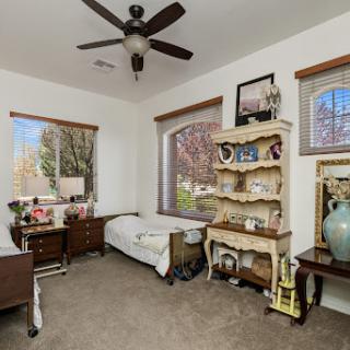 A cozy and well-decorated bedroom featuring a ceiling fan, natural light from large windows, and stylish furniture.