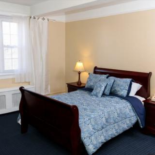A cozy bedroom with a wooden bed, a bedside lamp, and a window with white curtains.