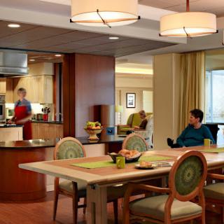 A cozy interior featuring a dining area and kitchen, with one person cooking and another relaxing.