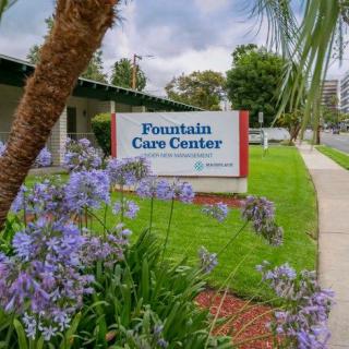 Entrance sign of the Fountain Care Center surrounded by lush greenery and purple flowers.