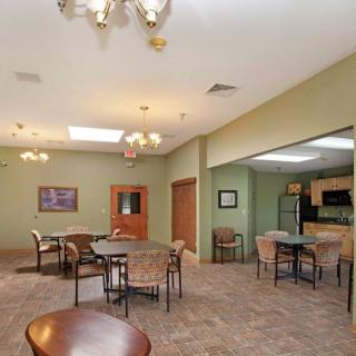 A spacious dining area with tables and chairs, adjacent to a kitchen in a community room.