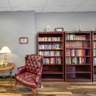 A cozy reading nook featuring bookshelves, a leather chair, and a table lamp.