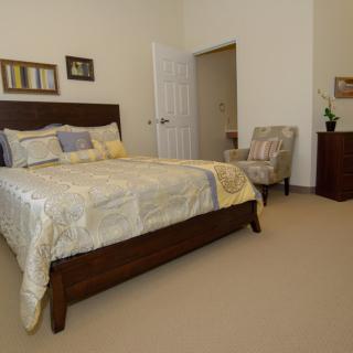 A cozy bedroom with a neatly made bed, an armchair, and a small dresser.