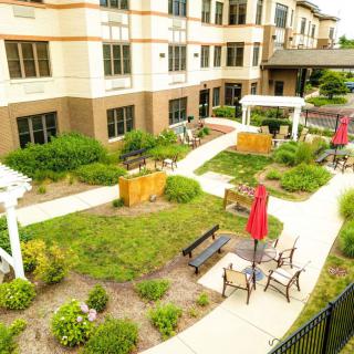 A well-maintained garden area with benches and umbrellas near a residential building.