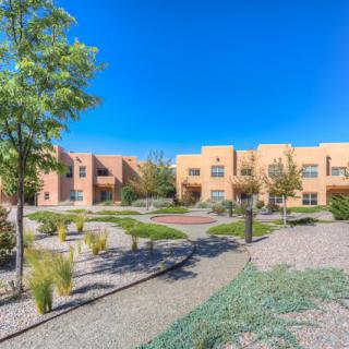 A modern apartment complex with landscaped pathways and desert-style architecture under a clear blue sky.