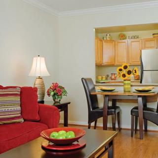 A cozy living room with a red sofa and a view into the kitchen area, featuring warm wooden accents and modern decor.