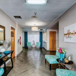 A modern hallway with a waiting area featuring chairs, artwork, and decorative flowers.