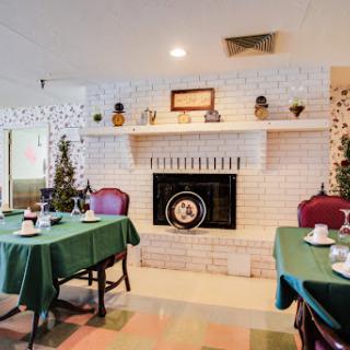 A cozy dining room featuring a white brick fireplace and tables set with green tablecloths.
