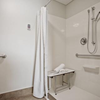An accessible bathroom with a shower area featuring grab bars, a shower bench, and a white curtain.