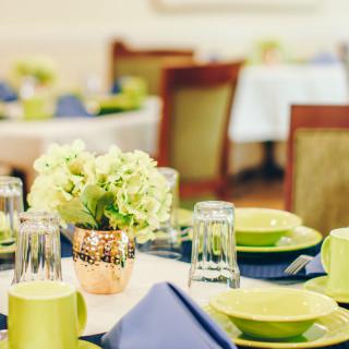 A beautifully set dining table with green dishes, blue napkins, and a floral centerpiece.