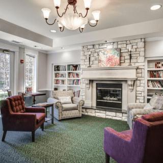 A cozy living room with a fireplace, surrounded by bookshelves and comfortable armchairs.