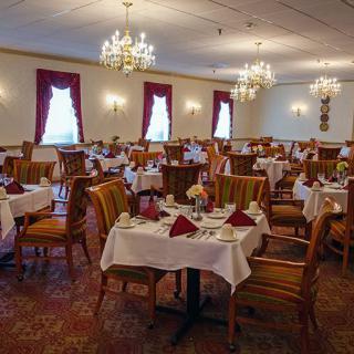An elegant restaurant dining room with neatly arranged tables and chairs, adorned with chandeliers and red curtains.