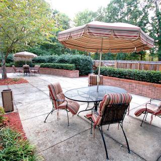 An inviting outdoor patio area with a table and chairs under umbrellas, surrounded by lush greenery.