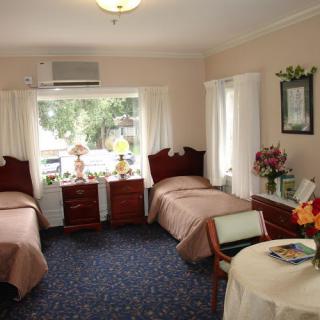 A cozy bedroom with two twin beds, featuring elegant decor and a large window with curtains.