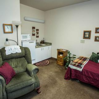 A cozy and compact living space featuring a bed, armchair, and small kitchenette.