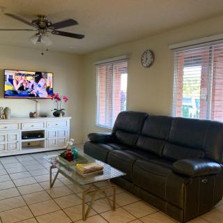 A cozy living room with a leather sofa, a TV mounted on the wall, and a glass coffee table.